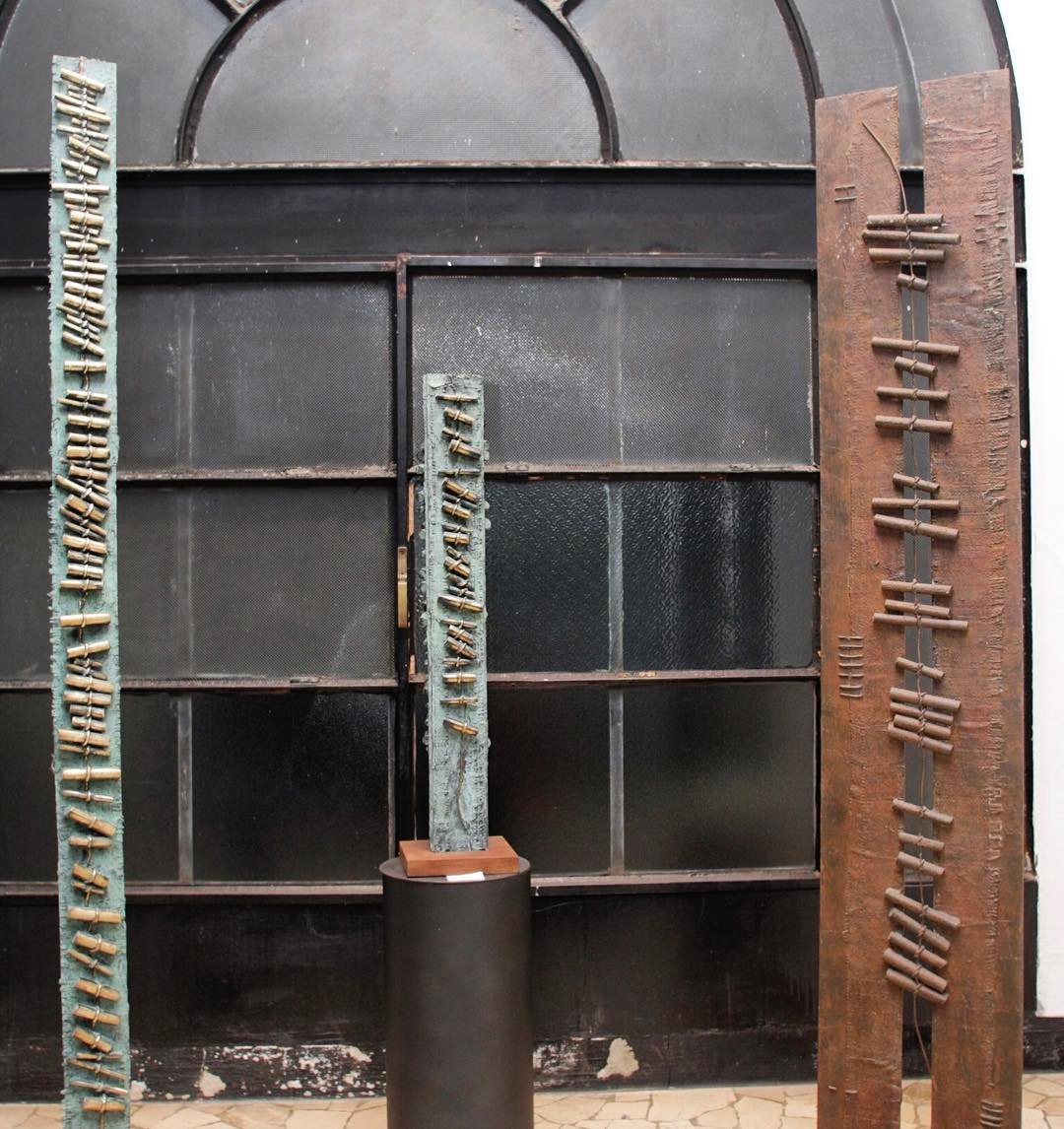 Tall Sentieri sculptures displayed in front of the arched windows of Fornace Curti